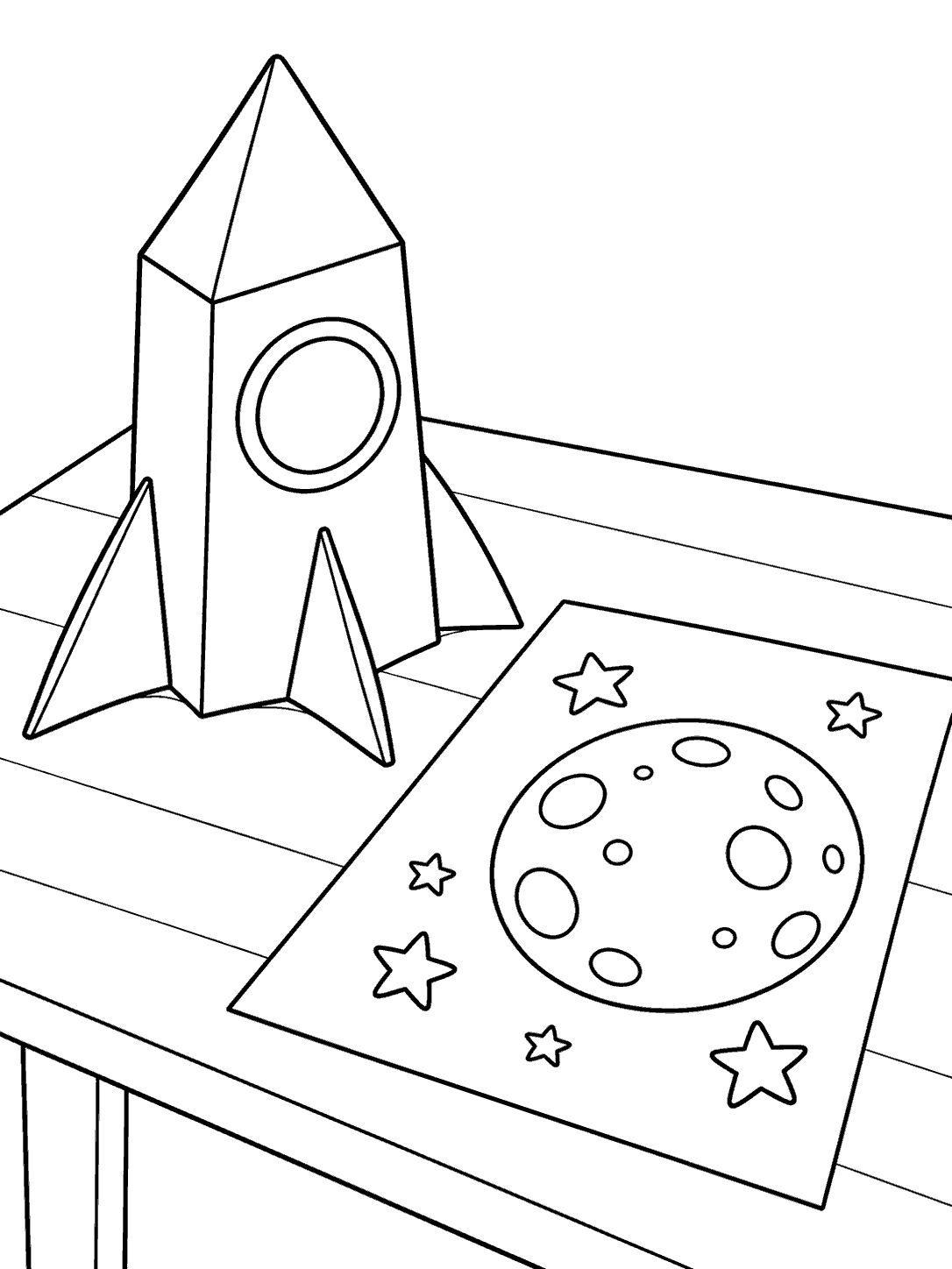 Black outline coloring page of a folded paper rocket beside a sheet showing an outlined moon and stars on a tabletop.